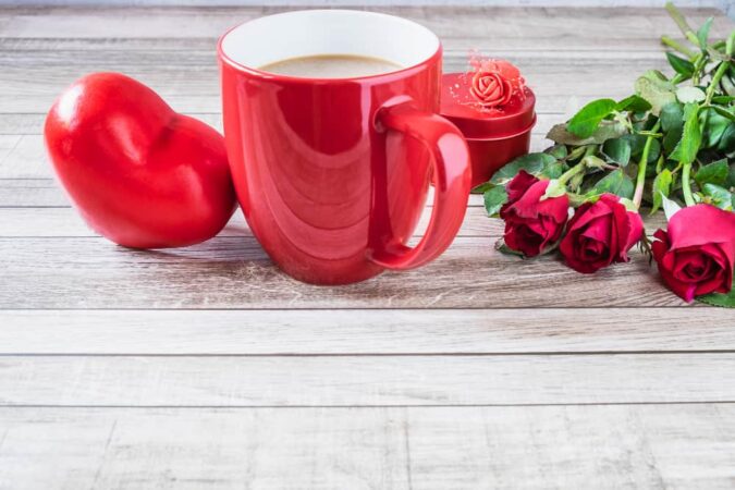 Une tasse à café rouge vif avec un cœur décoratif, des roses rouges et une boîte-cadeau romantique.