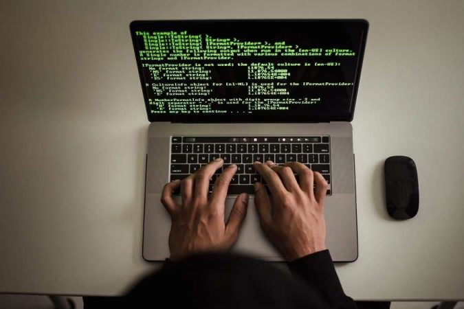 Une vue de dessus montre deux mains tapant sur le clavier d'un ordinateur portable affichant des lignes de code vertes.