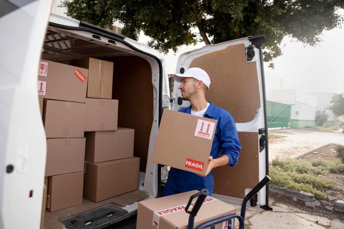 Un déménageur professionnel charge des cartons étiquetés fragile dans un camion utilitaire pour montrer comment organiser un déménagement de dernière minute en urgence.