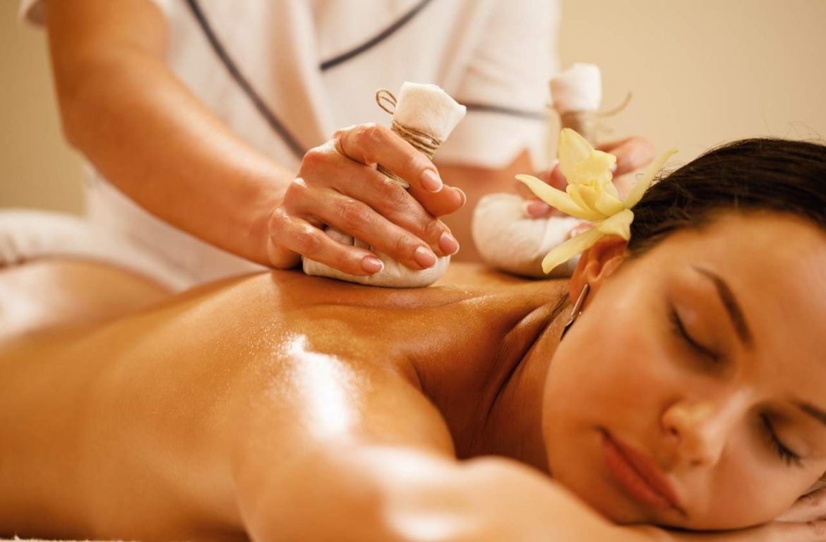 Une femme détendue reçoit un soin aux pochons d'herbes illustrant l'expérience d'un massage ayurvédique abhyanga origines et bienfaits.