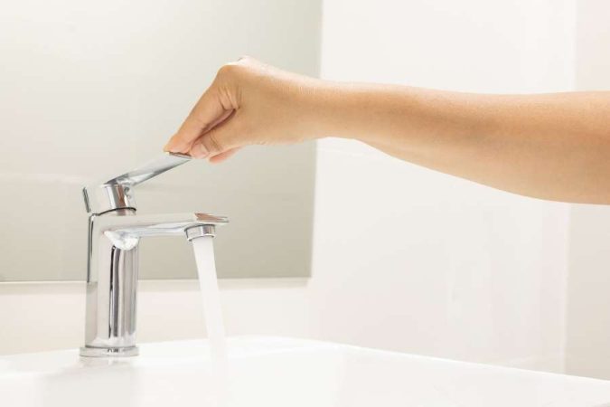 Une main manipule le levier d'un mitigeur de lavabo chromé pendant que l'eau coule.