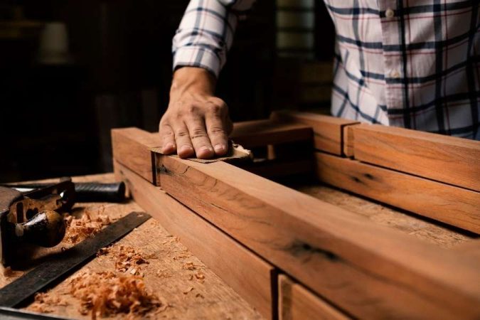 Un artisan ponce manuellement une pièce de bois avec du papier de ponçage fin dans un atelier.